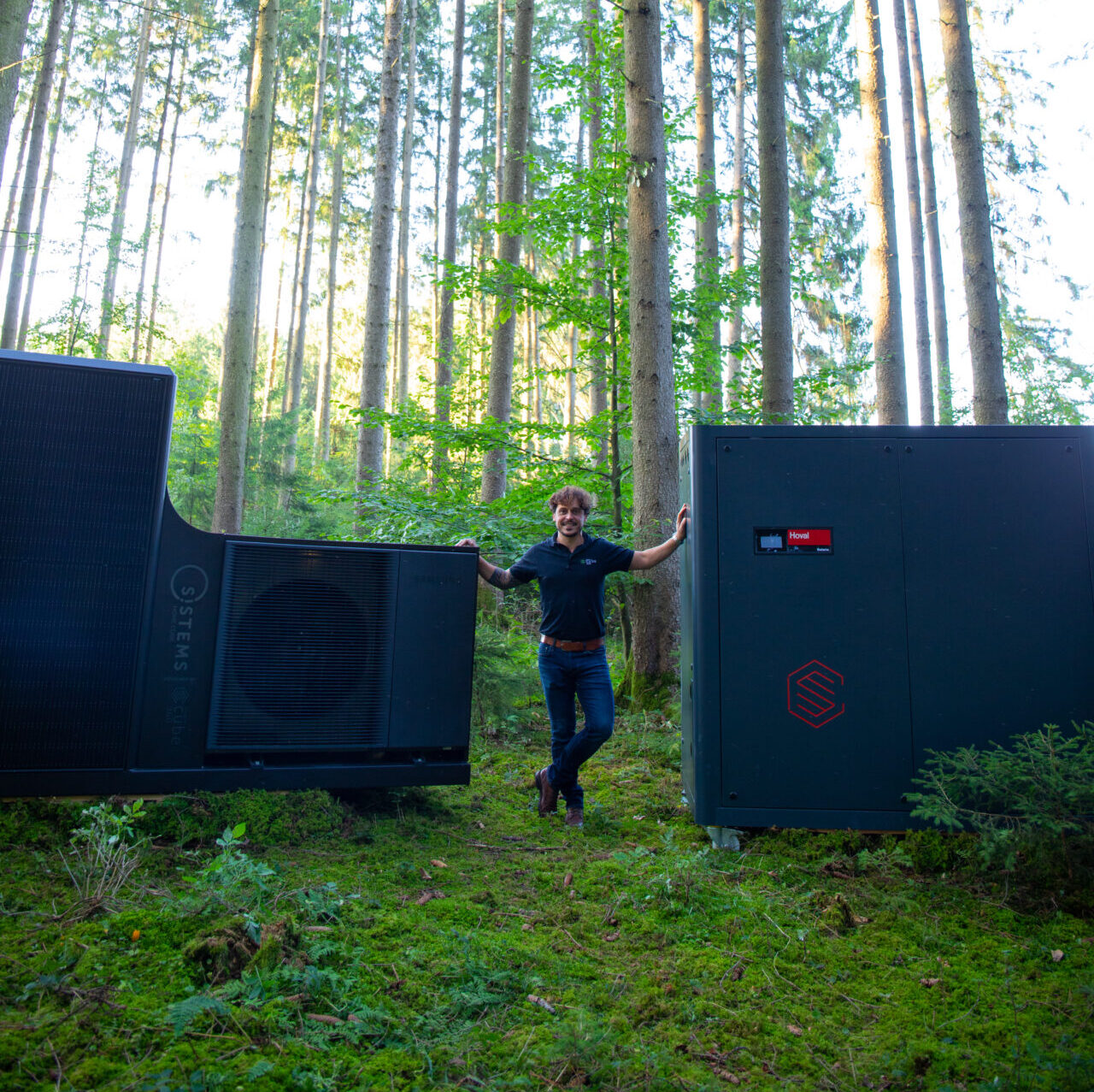 Geschäftsführer Thomas Kirner steht zwischen dem HOME CUBE (Heizzentrale inkl. Wärmepumpenaußeneinheit für draußen) und dem HEAT CUBE (kompakte Heizzentrale vorgefertigt für Innenbereich)